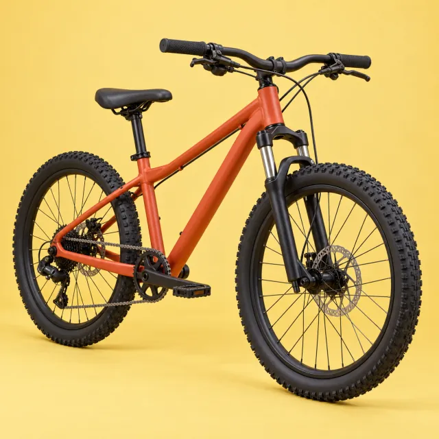 Bicicleta juvenil de 24 pulgadas con cuadro naranja, horquilla con suspensión y frenos de disco sobre fondo amarillo de estudio
