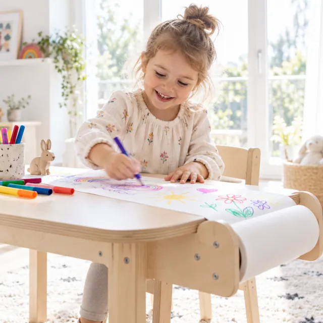 Niña dibujando con rotuladores sobre papel de rollo en una mesa infantil de contrachapado de abedul a contraluz